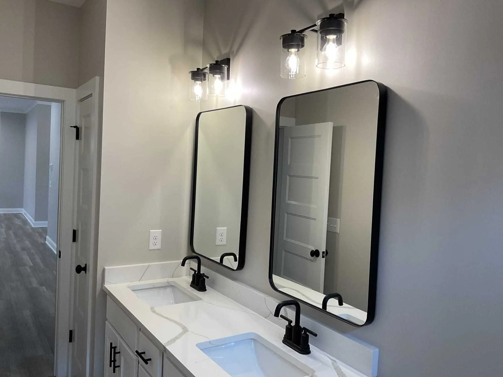 Bathroom with two mirrors, sinks, and black fixtures. Gray walls, white countertop, and modern lighting.