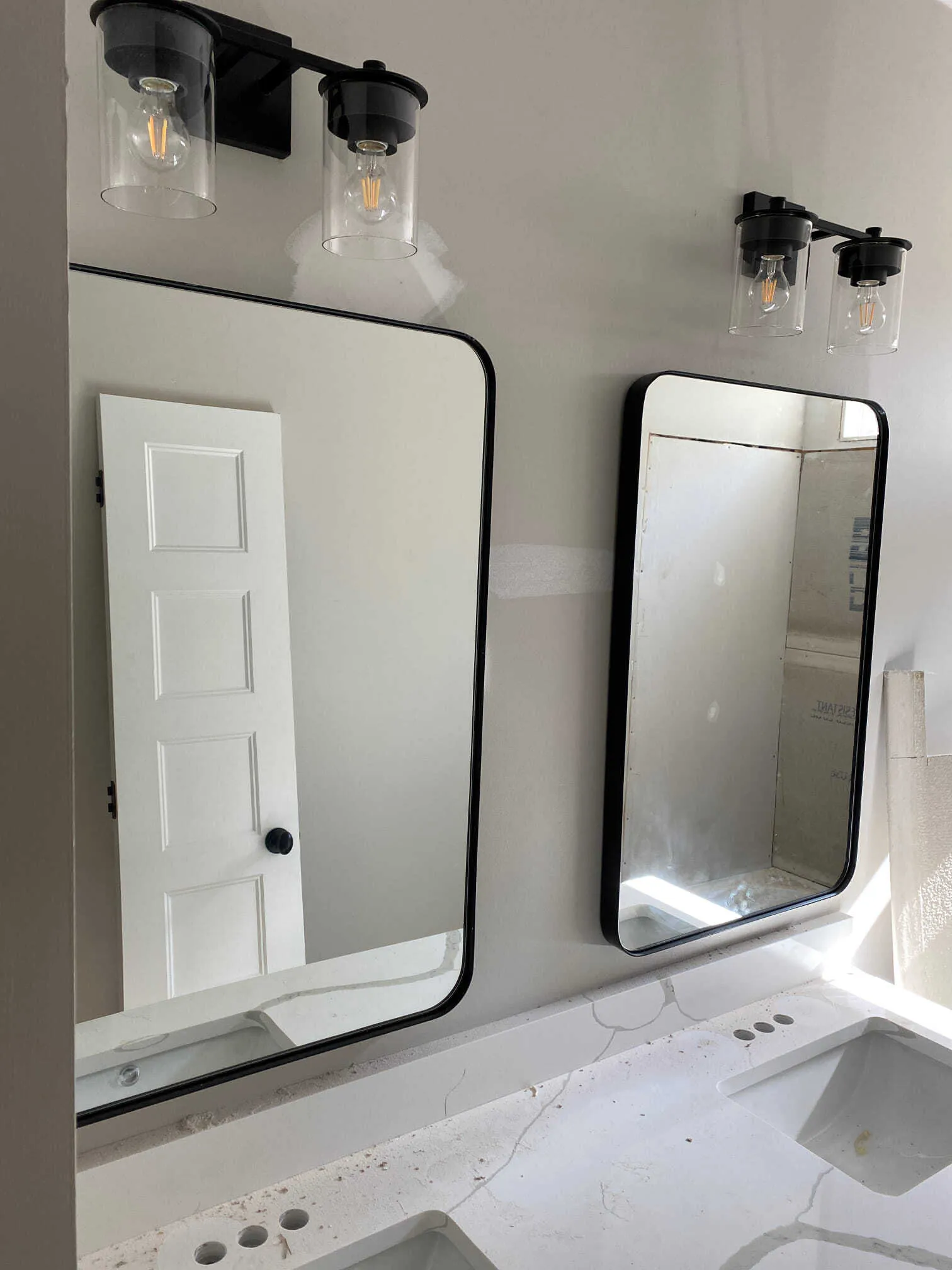 Two bathroom mirrors above a countertop, each with a black-framed light fixture.