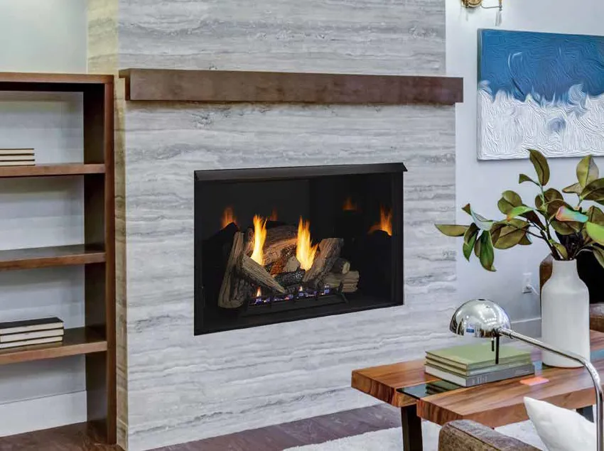 A gas fireplace with a wooden mantel and gray stone surround, adjacent to a wooden bookshelf and a c…