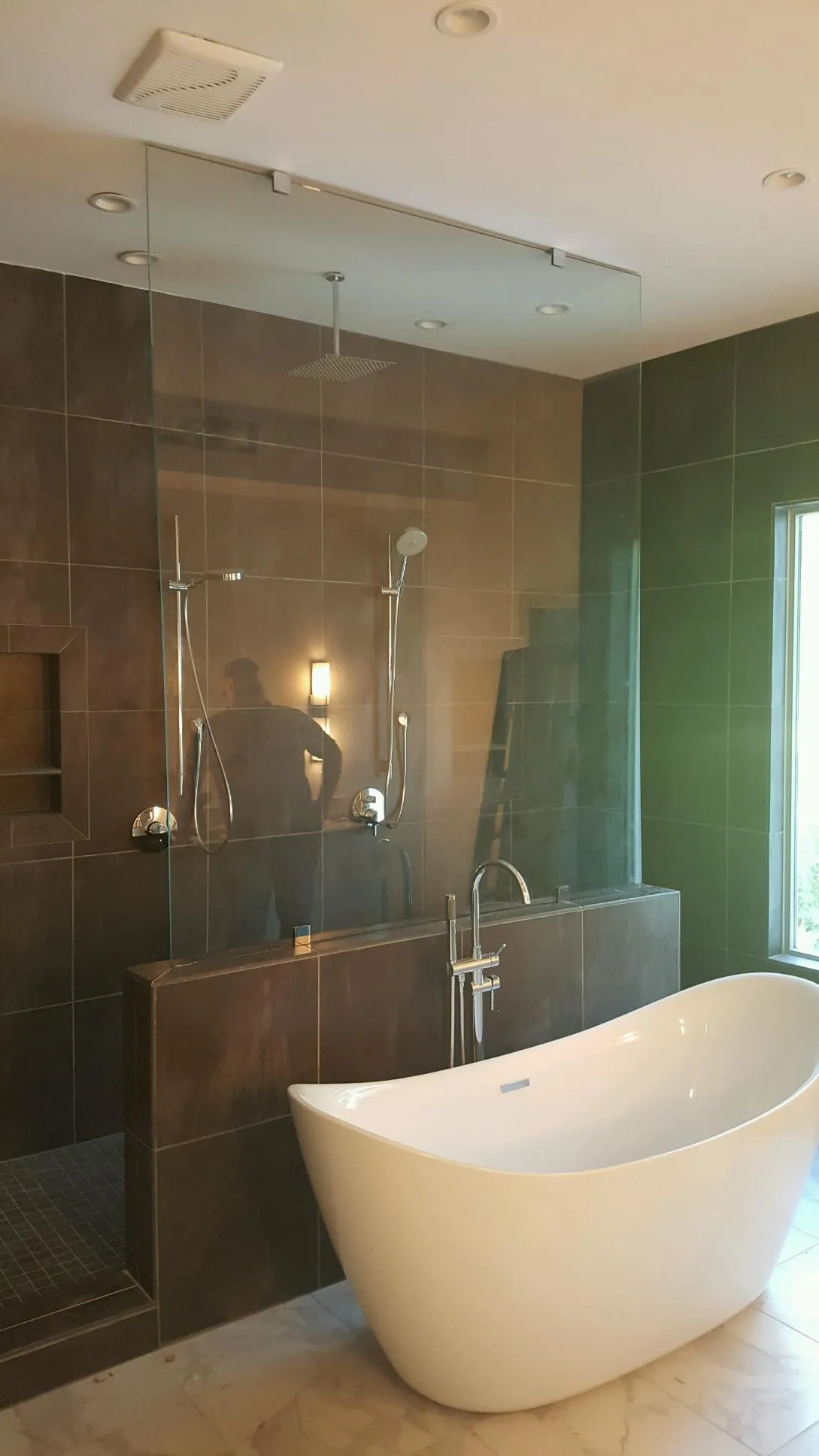 Modern bathroom with a white freestanding tub, glass shower, and dark brown tile walls.