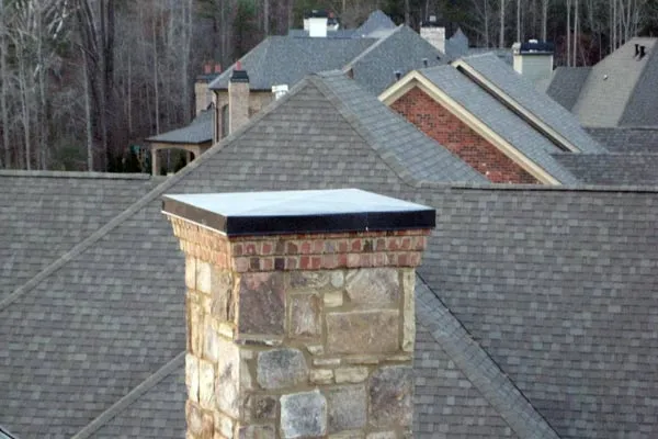 Brick and stone chimney on a shingled roof, other houses in the background.