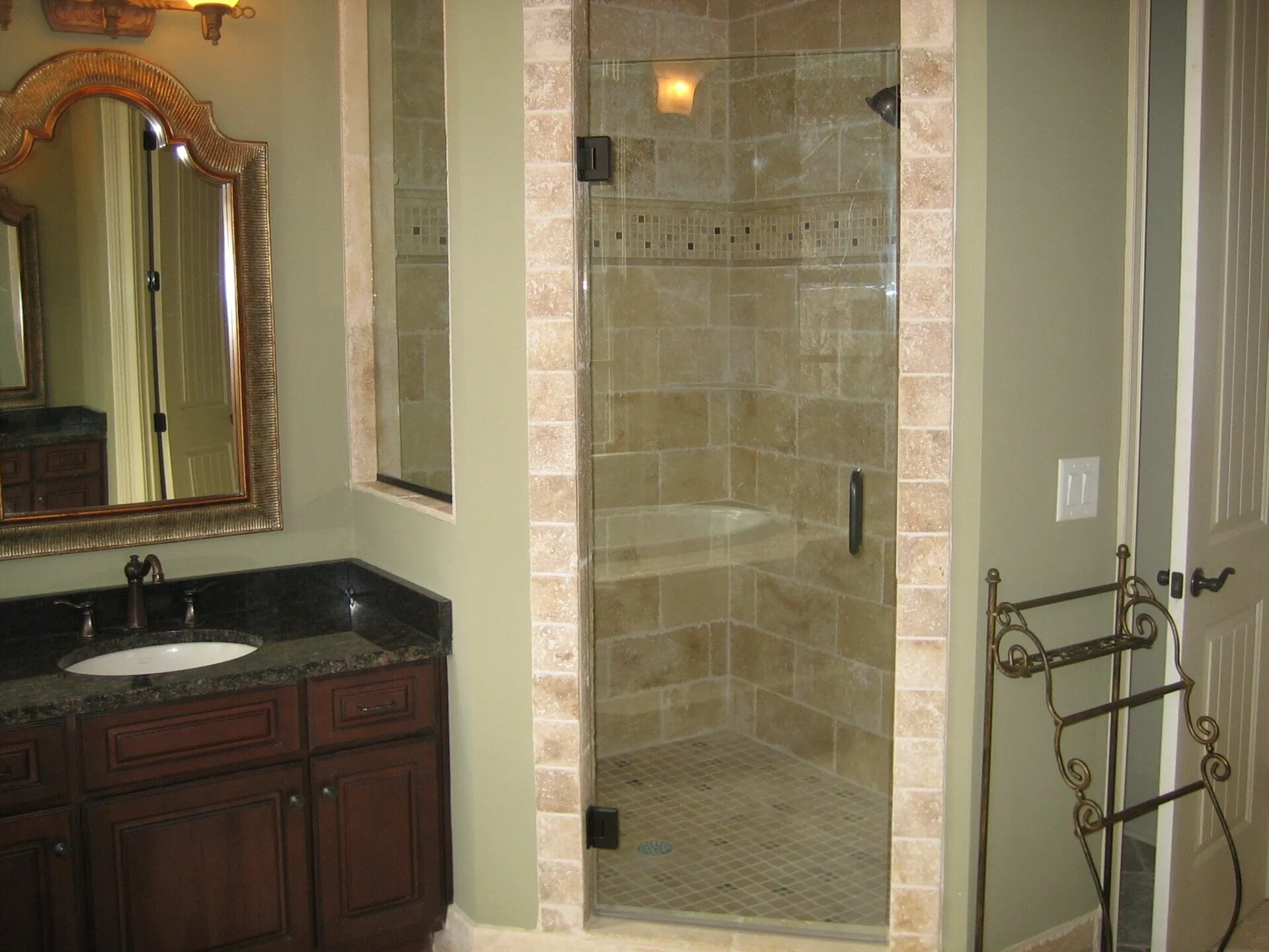 Bathroom with dark wood vanity, stone shower with glass door, and ornate mirror.