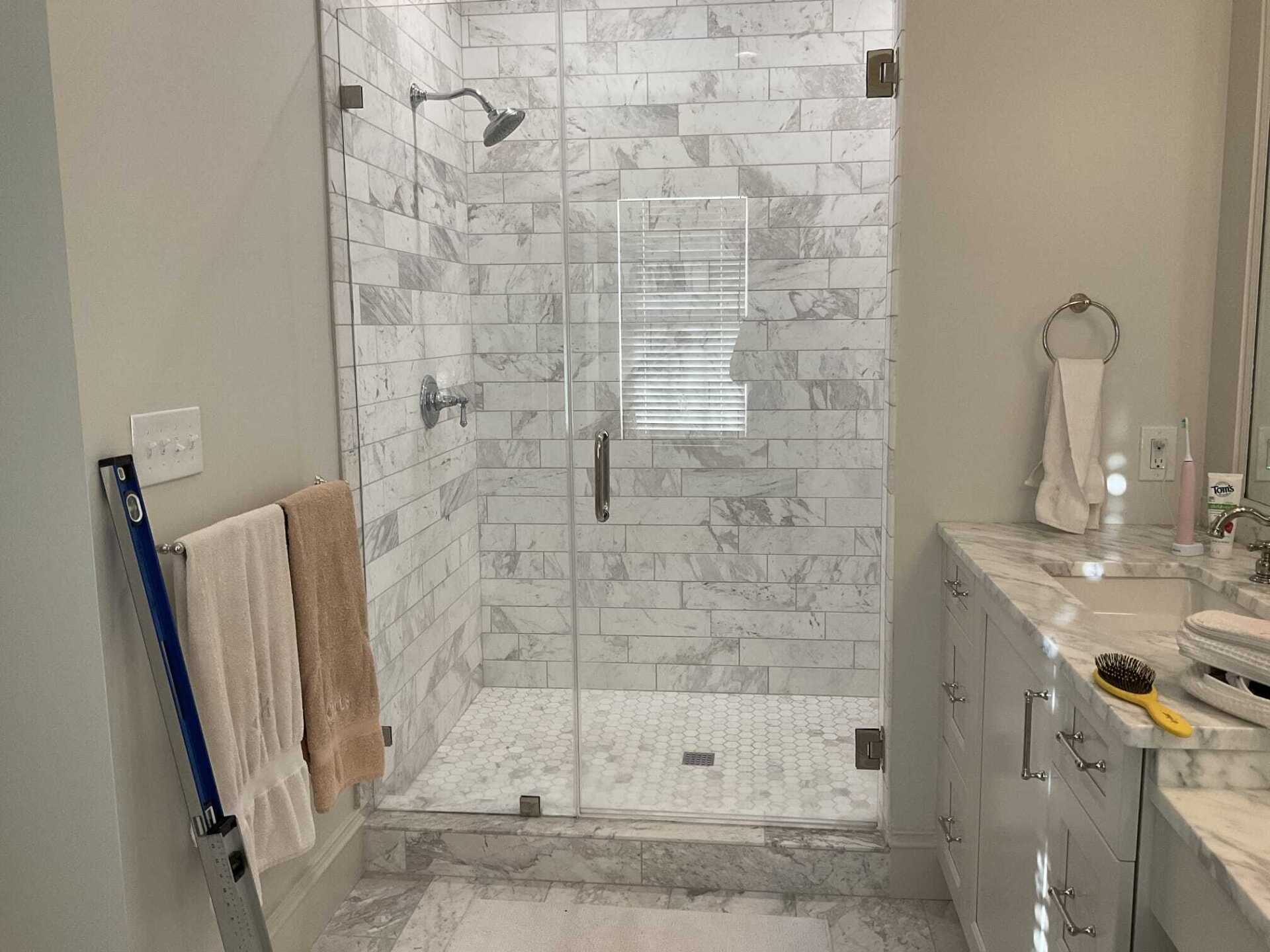 Bathroom with glass shower door, marble tile walls, white cabinets, and towels hanging.
