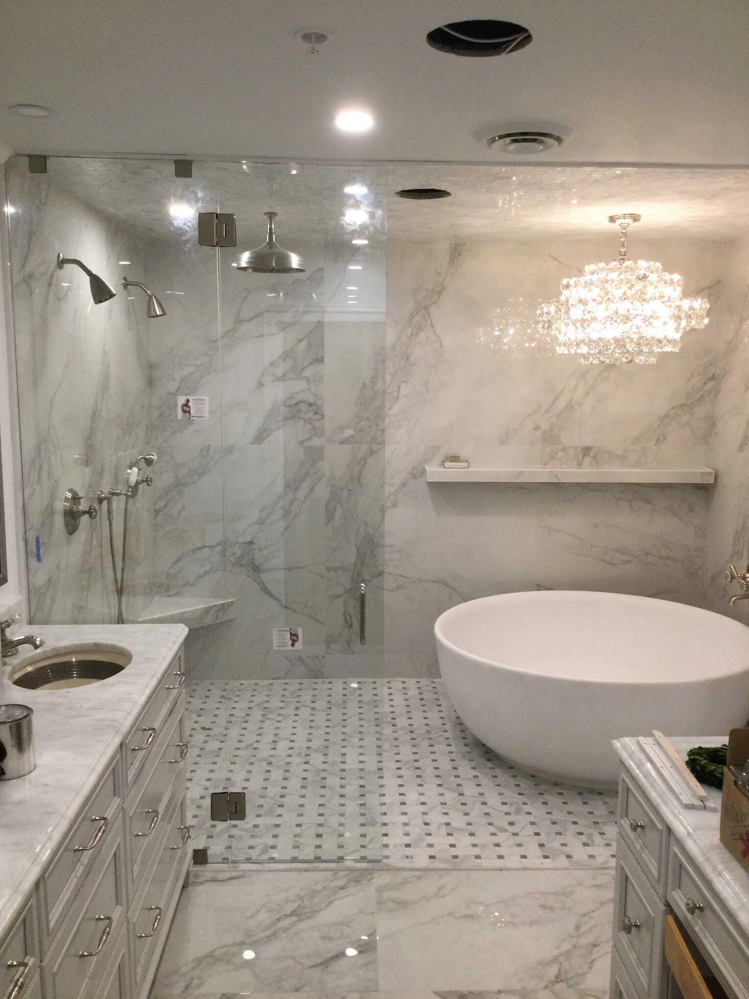 Luxurious bathroom with marble walls and floors, a glass shower, a soaking tub, and a chandelier.