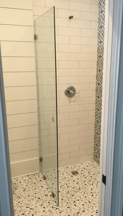 Shower with glass door, white brick tile, patterned accent wall, and terrazzo floor.