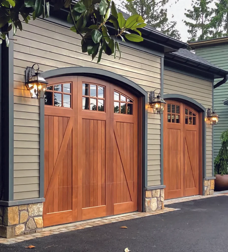 Two wooden garage doors with arched tops, glass panels, and sidelights. Green siding, stone accents,…