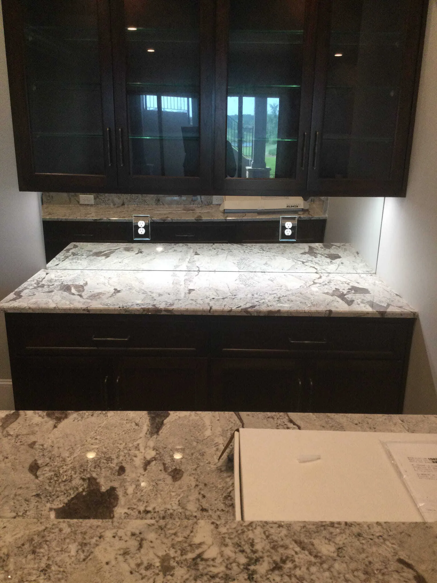 Dark wood cabinet with glass doors, granite countertop, and under-cabinet lighting.