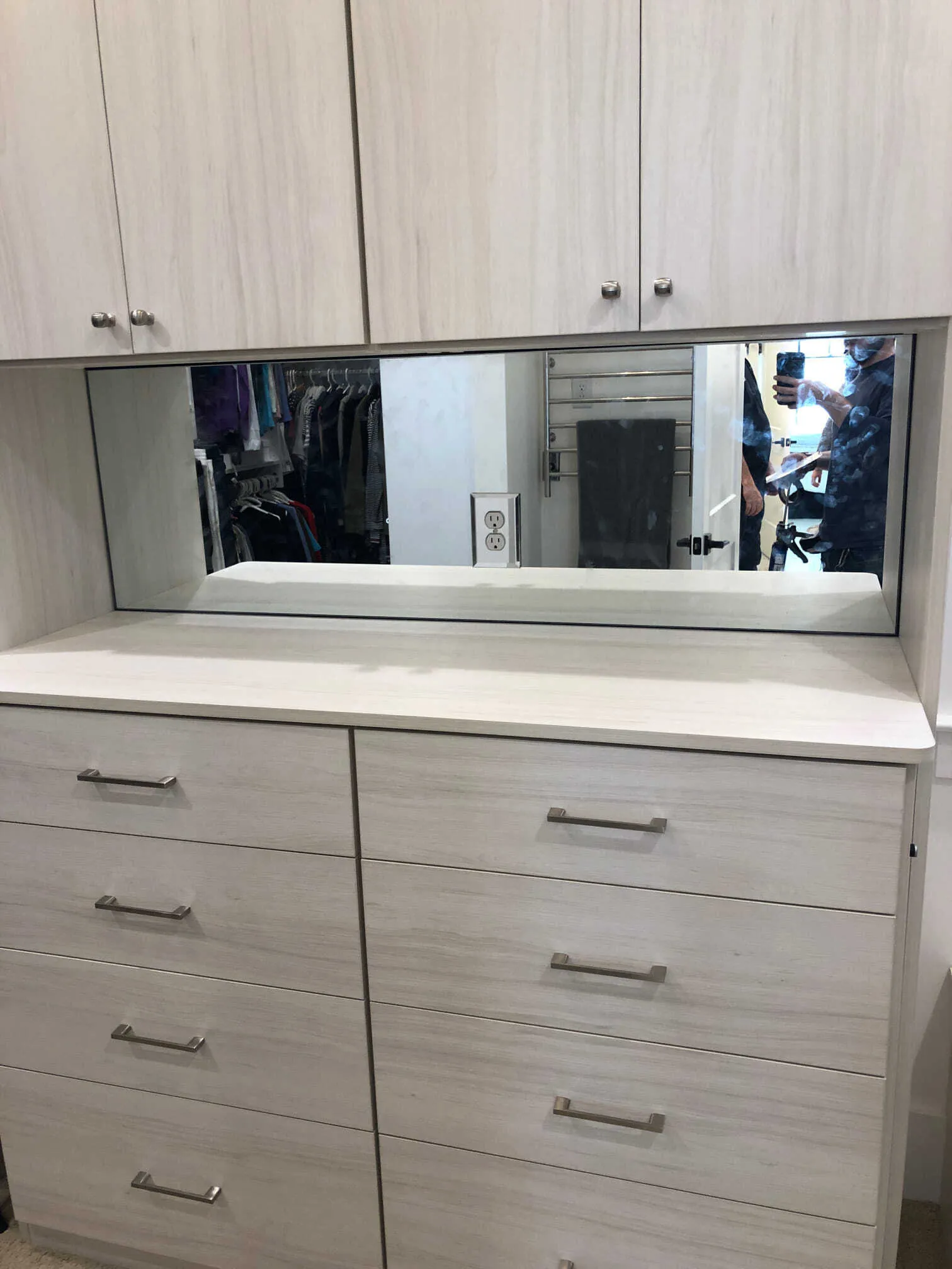 Light-colored wooden dresser with eight drawers and an integrated mirror, located in a walk-in closet.