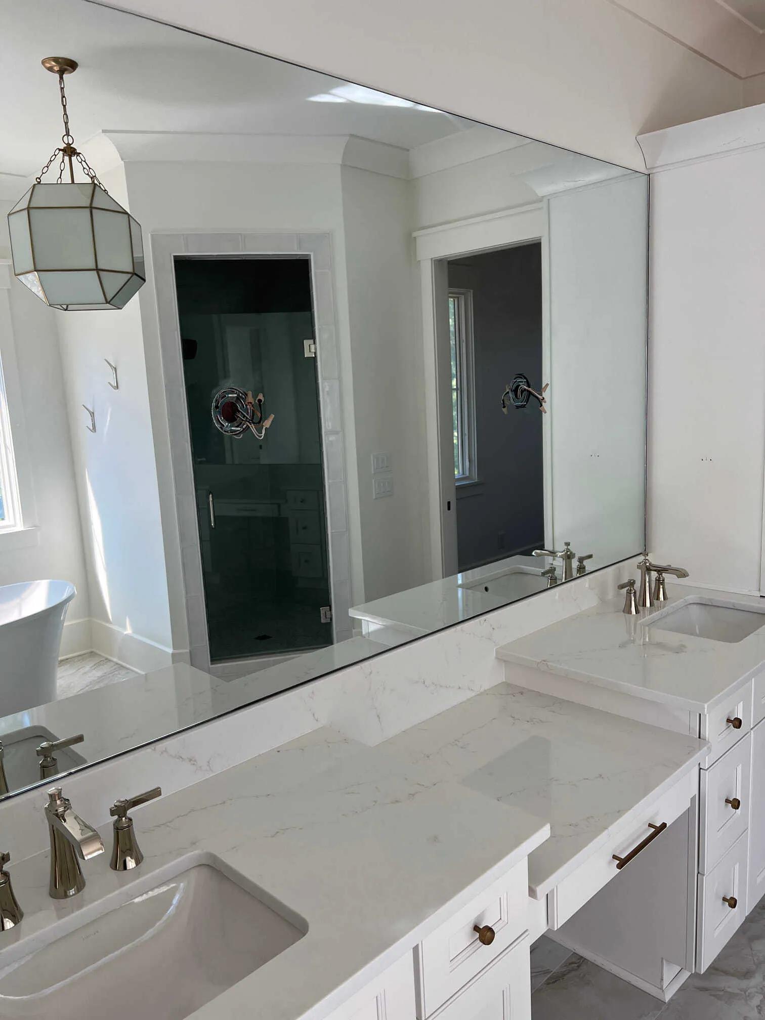 A bright bathroom vanity with a large wall mirror, white cabinets, marble-patterned countertops, and hanging lantern light.