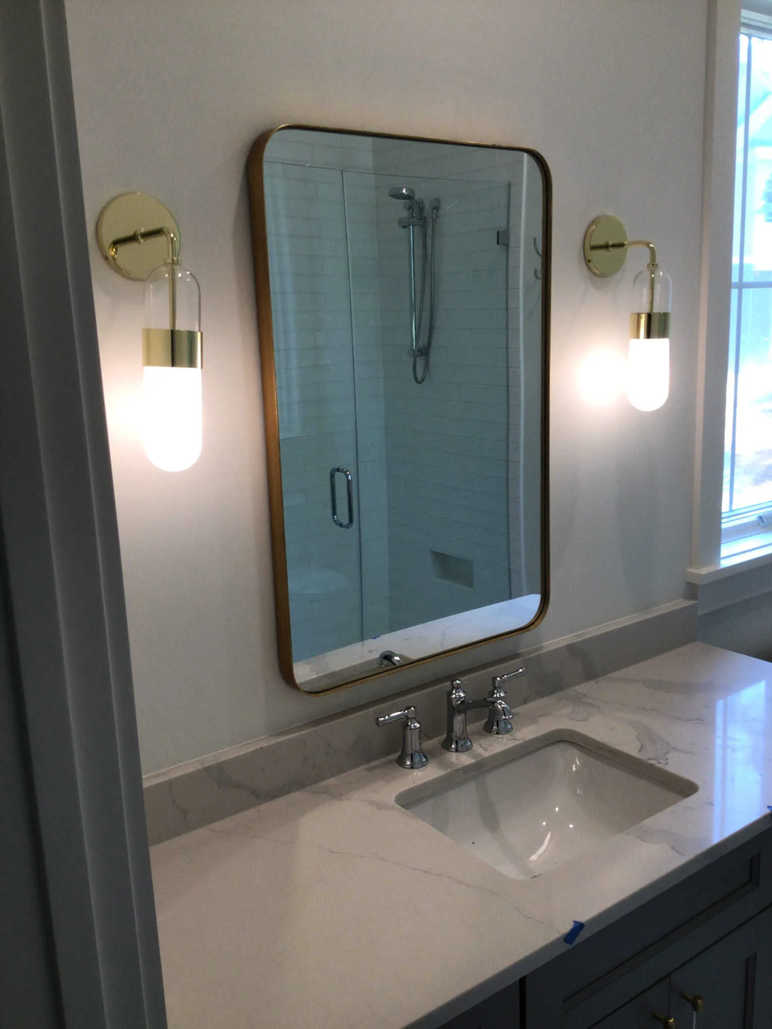 Bathroom vanity with a gold-framed mirror, two sconces, a sink, and a marble countertop.
