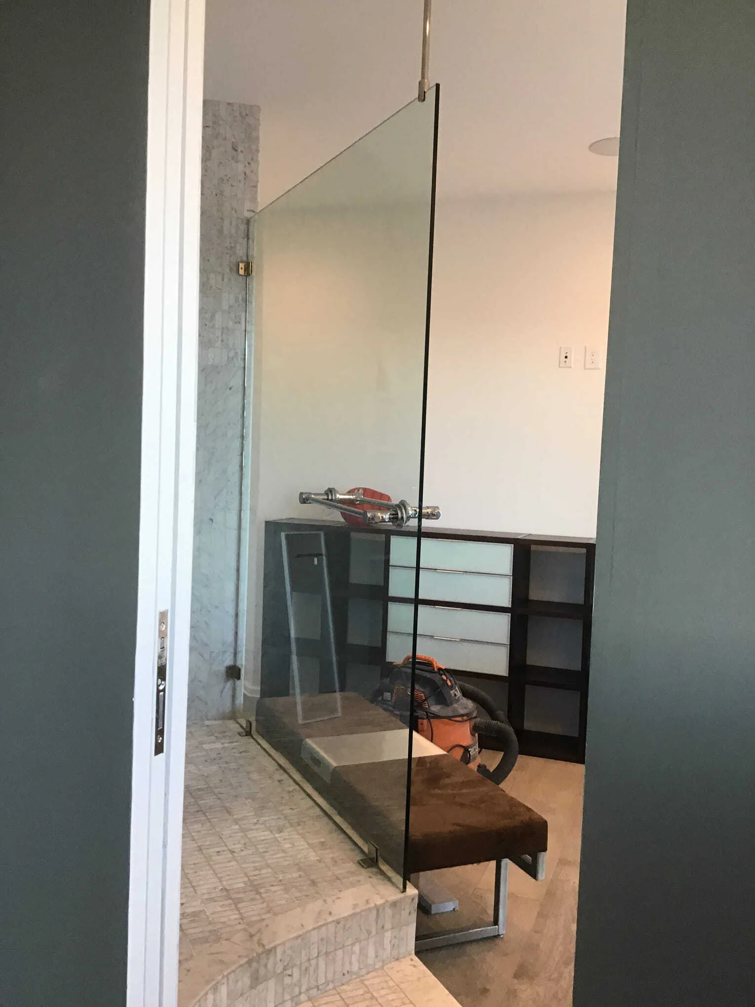Bathroom with glass shower panel, brown wooden bench, and gray walls.