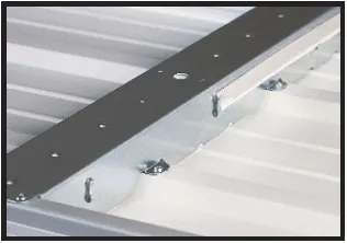 A metal bracket secured to a corrugated white metal roof with fasteners and a strip of foam insulati…
