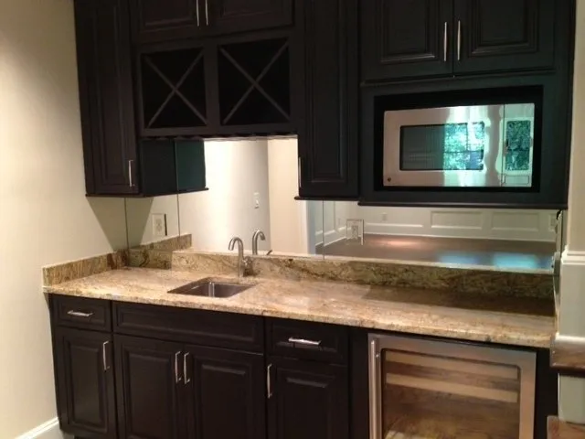A home wet bar with dark wood cabinets, tan granite counters, a small stainless steel sink, and a built-in microwave.